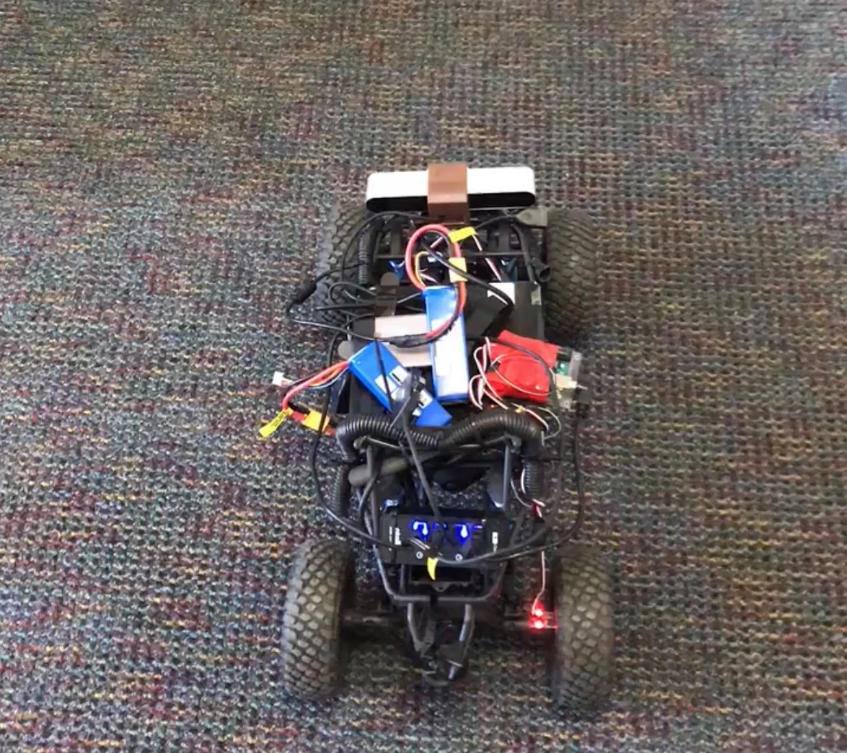 top view of RC car with camera and electronics. Video is of it driving in a hallway, avoiding the side walls